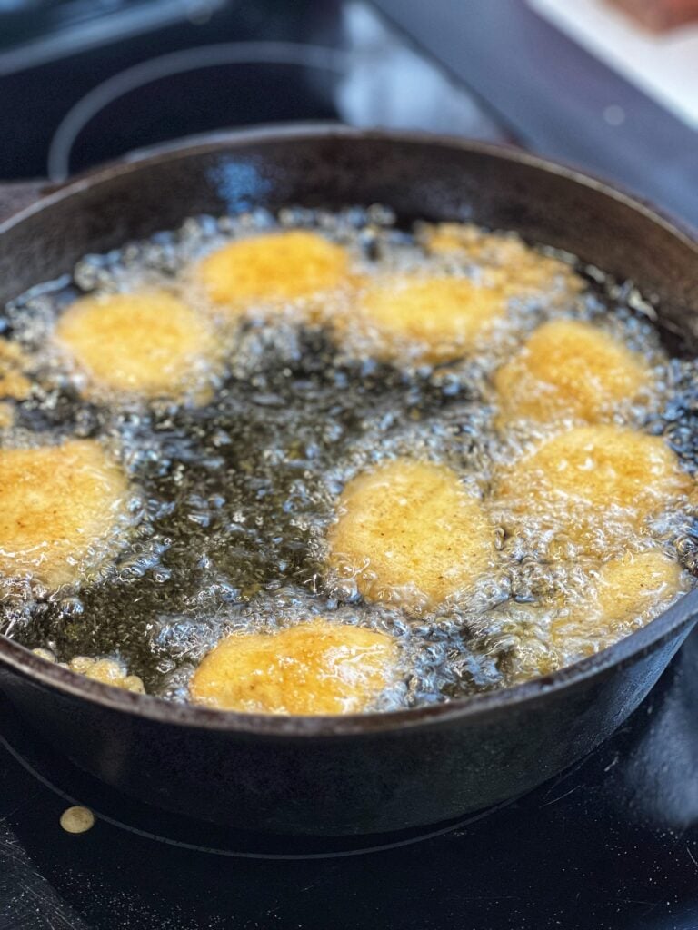 Chicken nuggets frying in a deep cast iron pot.