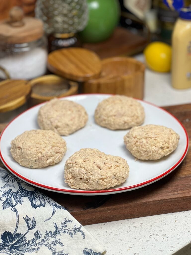 Five formed canned tuna patties on a white platter ready to be fried.