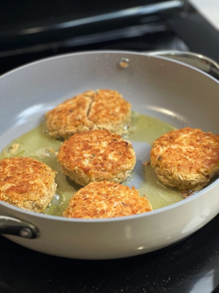 Pan frying five tuna patties in a non-stick pan.