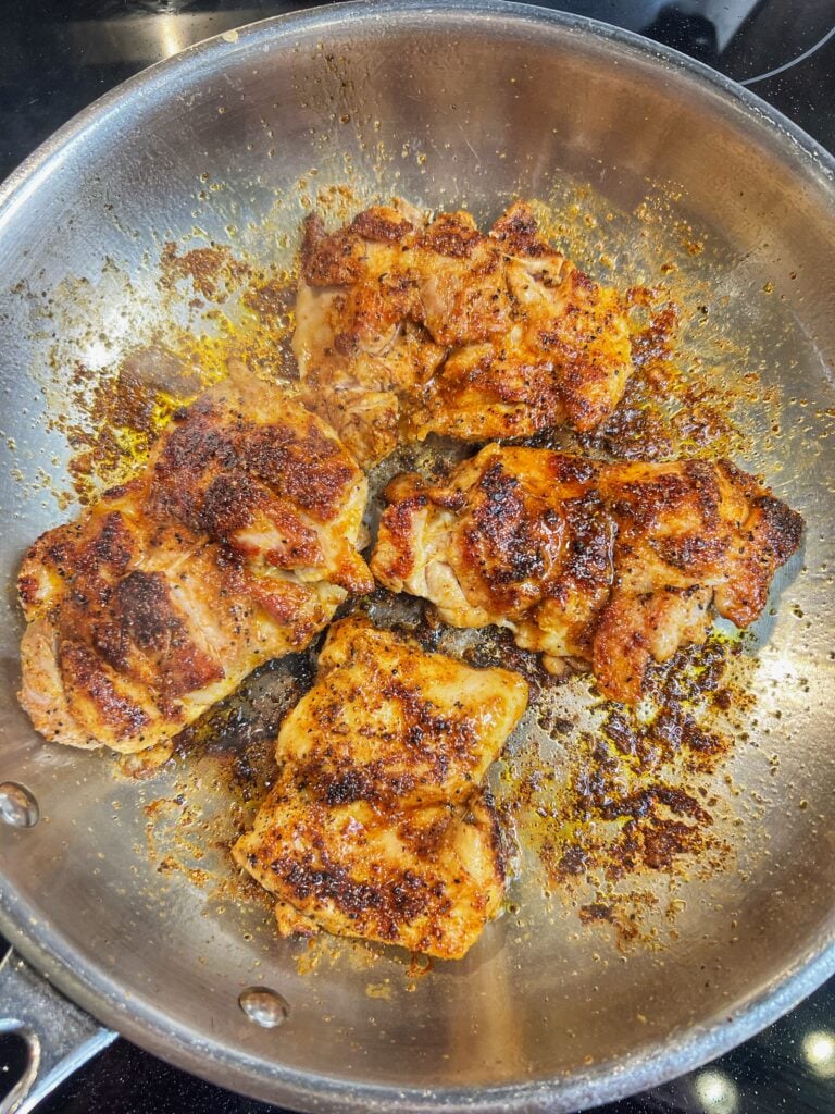 Four seasoned, boneless chicken thighs searing in a cast iron pan.