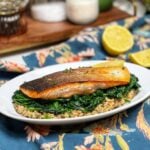 A piece of crispy skin salmon, showing with the skin side up. The salmon is sitting on top of a bed of farrotto and sautéed spinach.