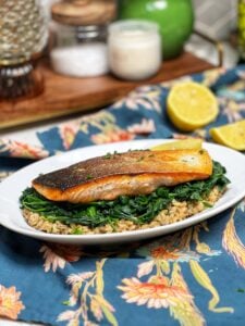 A piece of crispy skin salmon, showing with the skin side up. The salmon is sitting on top of a bed of farrotto and sautéed spinach.