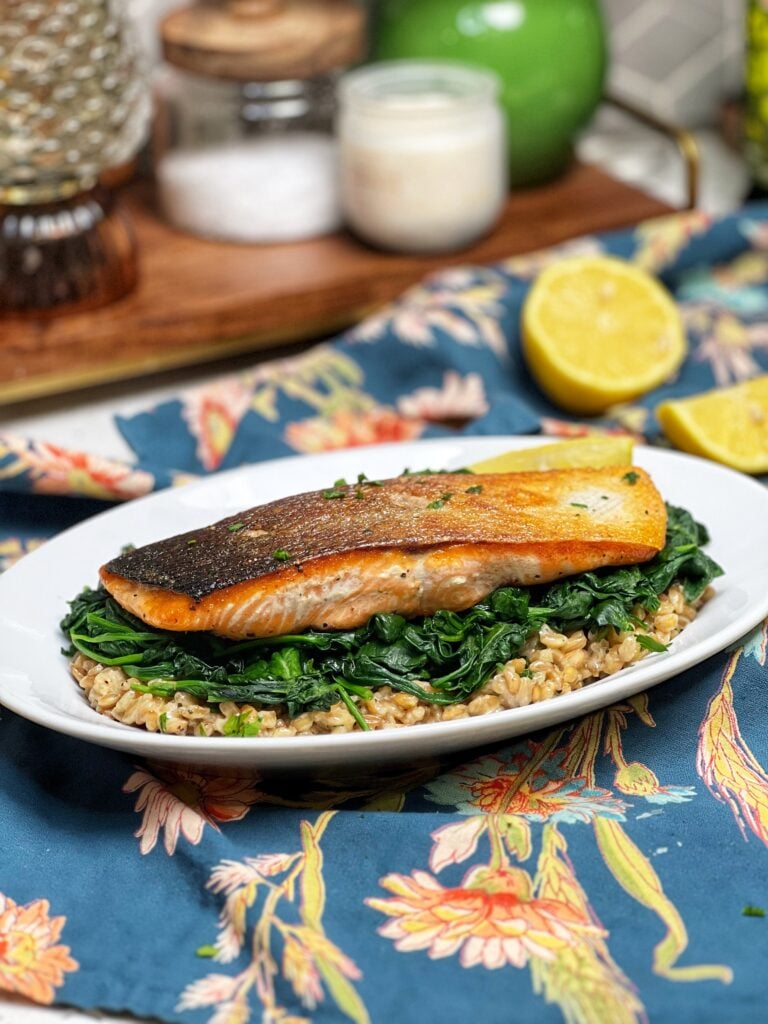 A piece of crispy skin salmon, showing with the skin side up. The salmon is sitting on top of a bed of farrotto and sautéed spinach.