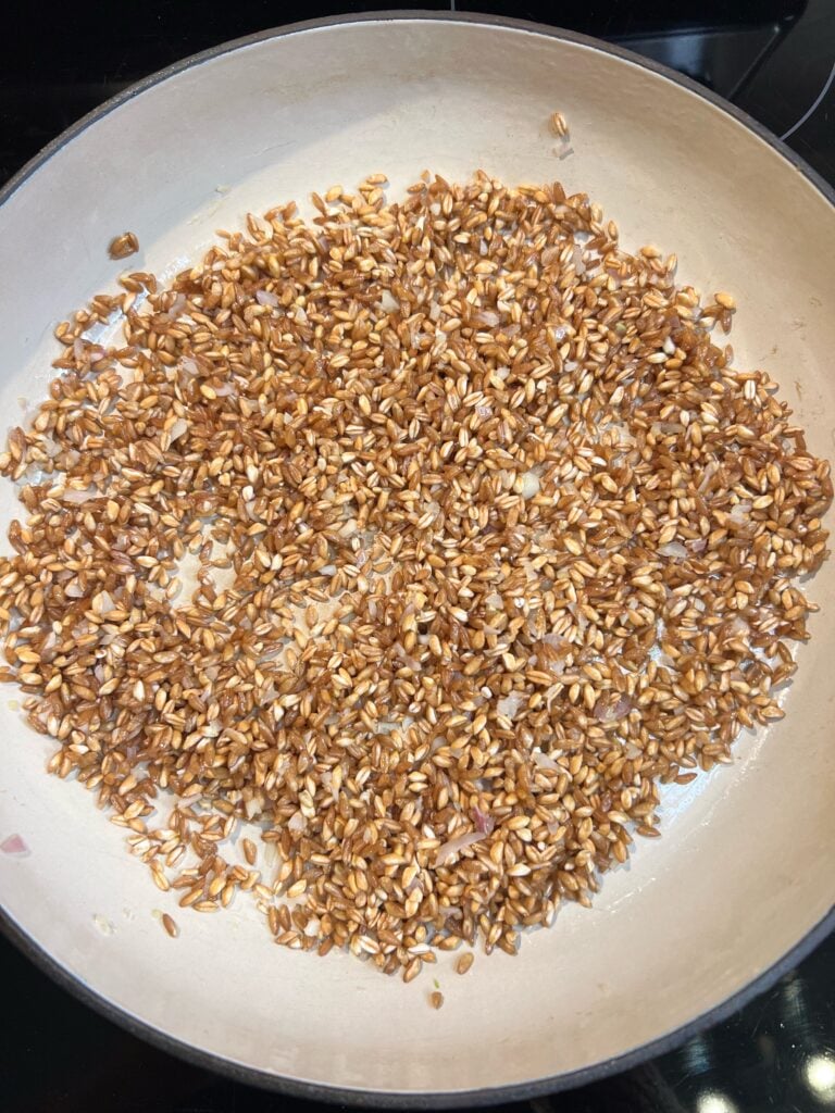 Farro toasting in a pan with minced shallots and garlic.