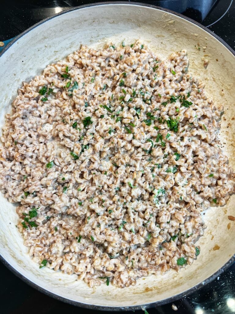 A pan of creamy Parmesan farro risotto. The dish is creamy and looks like risotto. It's garnished with fresh parsley.