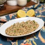 A white oval platter holding Creamy Parmesan Farro Risotto. The farro has a creamy brown appearance garnished with fresh chopped parsley.