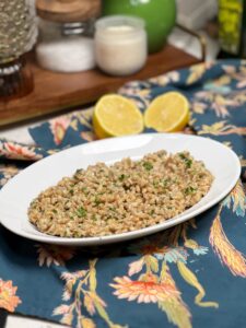 A white oval platter holding Creamy Parmesan Farro Risotto. The farro has a creamy brown appearance garnished with fresh chopped parsley.