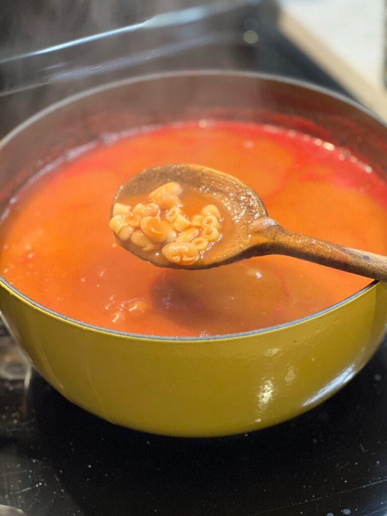 A pot of Italian Pasta Beans. Showing a spoonful of the pasta and beans with wooden spoon.