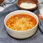 A white bowl of Italian Pasta Beans. The tomato based dish is filled with white beans and a ditalini pasta. The dish is topped with freshly grated Parmesan cheese.