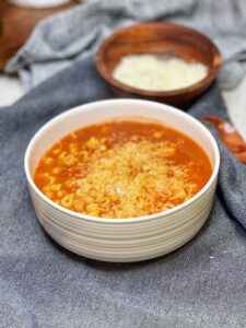 A white bowl of Italian Pasta Beans. The tomato based dish is filled with white beans and a ditalini pasta. The dish is topped with freshly grated Parmesan cheese.