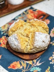 A round loaf of Easy Irish Soda Bread. The loaf was dusted with rice flour before baking and has a golden crust. It's sitting on a small wooden board.