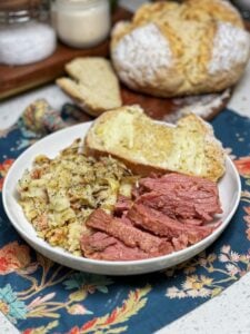A shallow white bowl filled with a St. Patrick's Day Dinner Idea of colcannon (mashed potatoes with cabbage and bacon), sliced corned beef and a slice of Irish Soda Bread