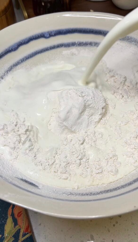 Pouring buttermilk into sifted flour in a bowl.