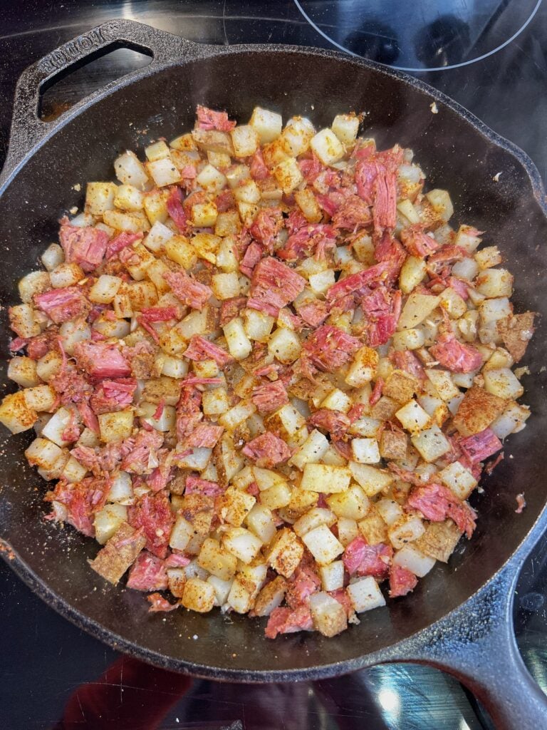 Diced corned beef in a cast iron pan with diced potatoes, and minced garlic and onions.