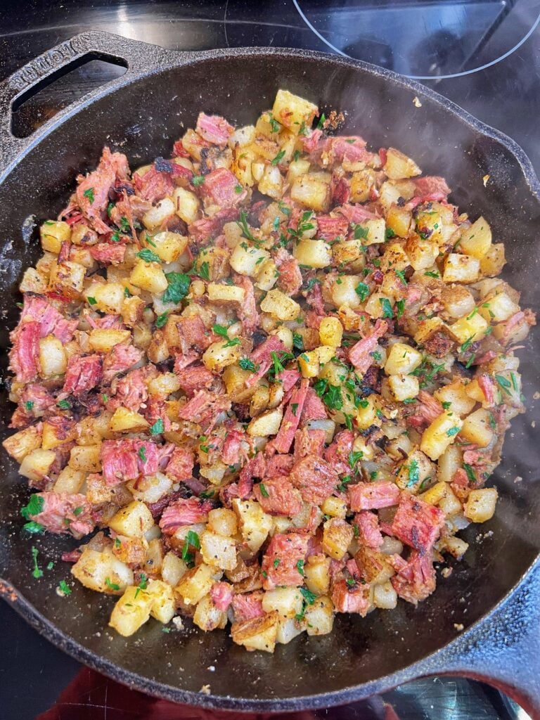 Crispy corned beef hash in a cast iron pan with diced potatoes and garnished with fresh parsley.