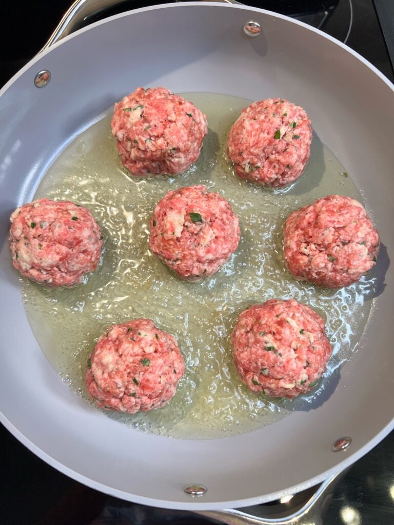 Frying seven large meatballs in light olive oil in a pan.