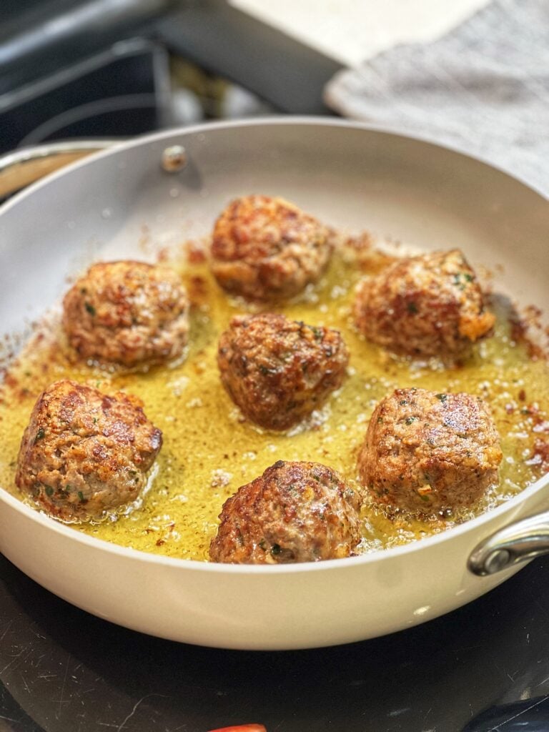 Seven browned meatballs in a pan with olive oil.