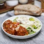 A meatball salad with simple vinaigrette. A bowl of salad topped with an open piece of burrata with three meatballs.