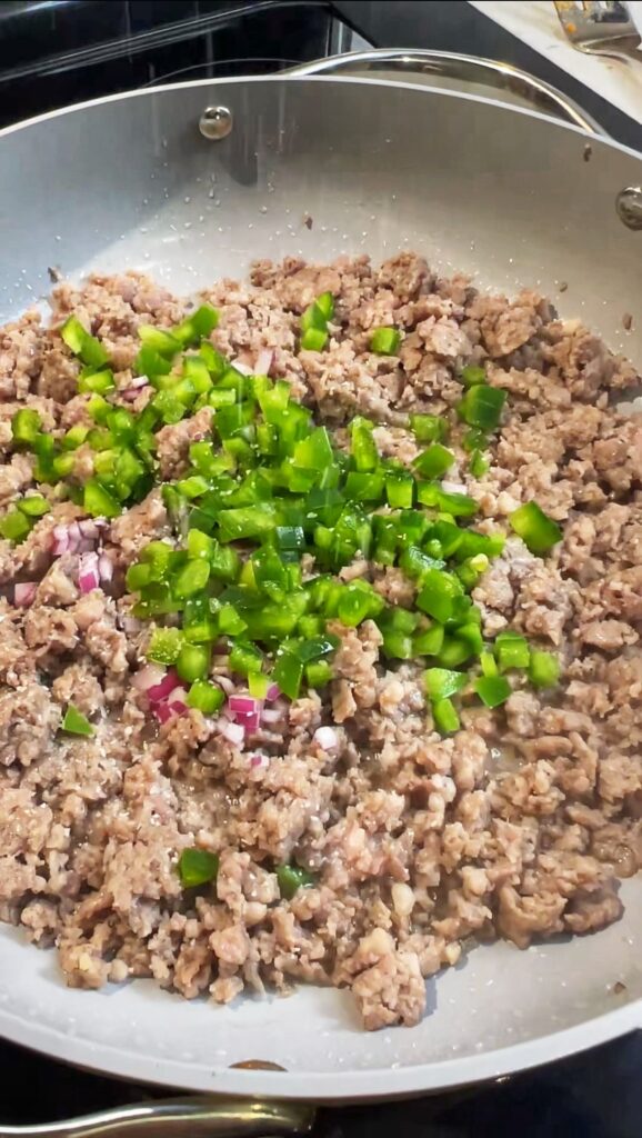 Ground breakfast sausage browning in a pan with diced onions and bell peppers.