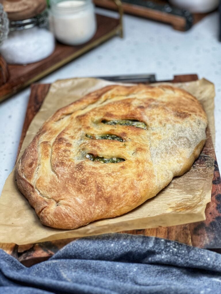 A whole mushroom cheese calzone with three slits on top. The calzone is browned from baking and sitting on a piece of brown parchment paper.