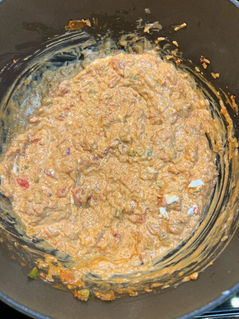 Cream cheese mixed with rice and tomatoes in a pot. The mixture has an orangish hue.