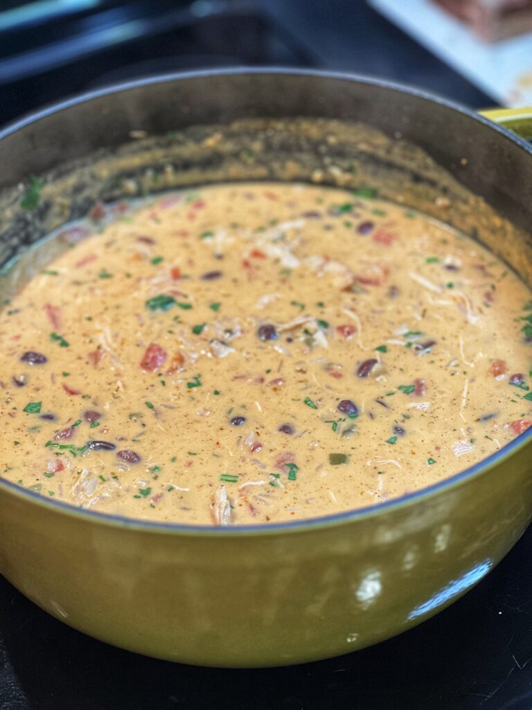 A pot of creamy taco soup. The soup contains shredded chicken, black beans, tomato and rice. The soup has a slight orangish hue.