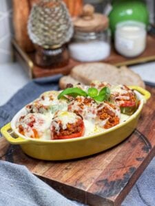 A yellow, oval casserole dish holding mini stuffed bell peppers. The peppers are filled with a tomato beef rice mixture and topped with melted mozzarella cheese.