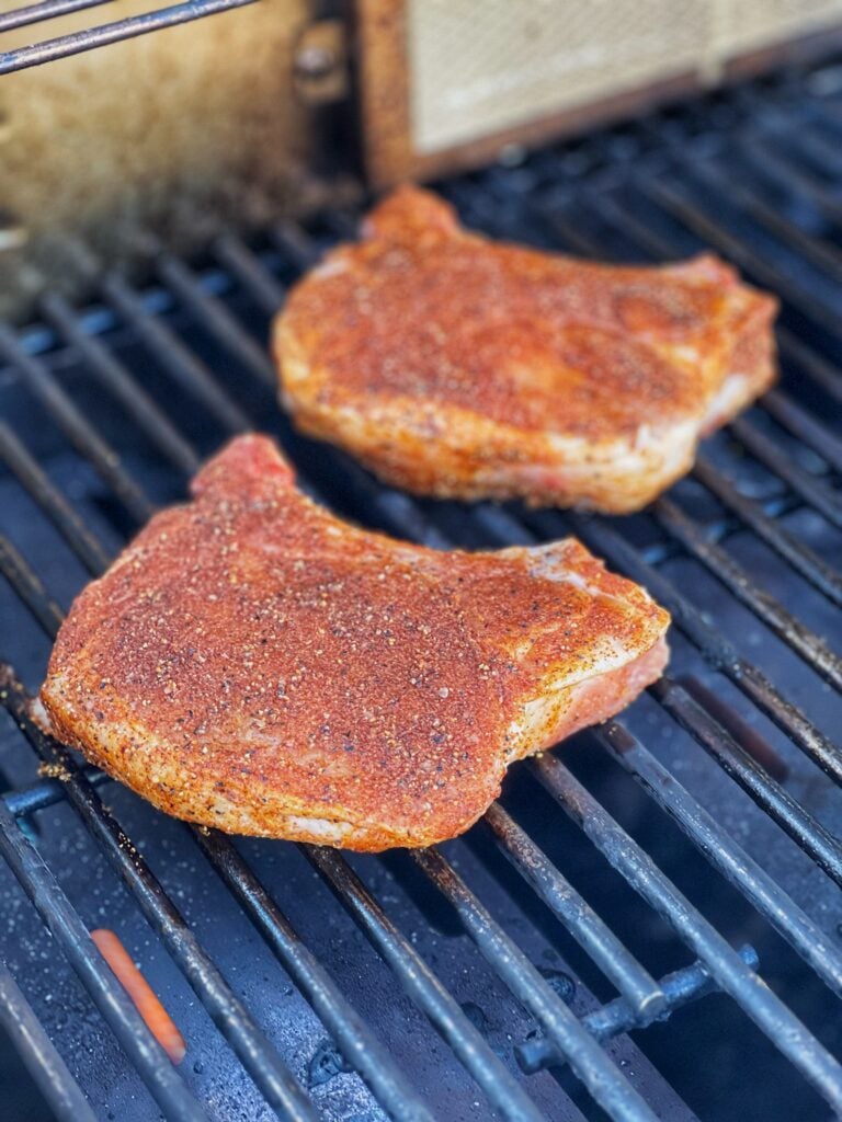 Two seasoned pork chops starting to cook on the grill.
