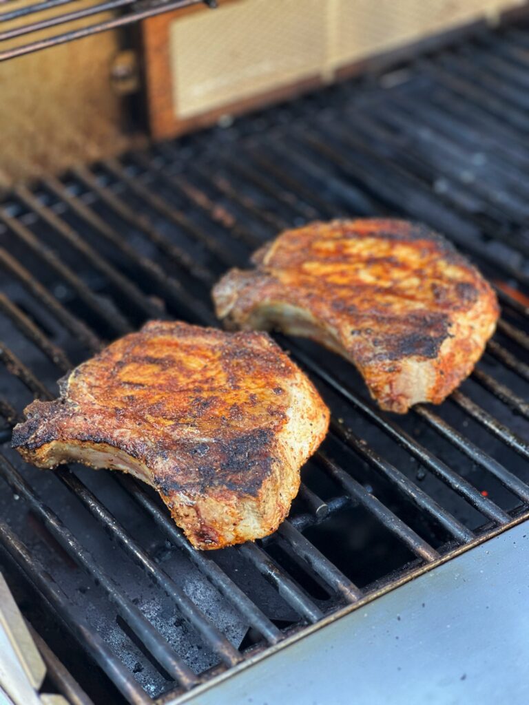 Two juicy grilled pork chops sitting on grill grates. The chops are thick with the bone-in.