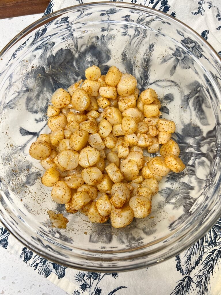 Bay scallops (tiny) in a glass bowl seasoned with Cajun seasoning.