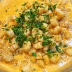 Seared bay scallops in a Cajun cream sauce. The sauce is orangish in color and the dish is garnished with fresh chopped parsley.