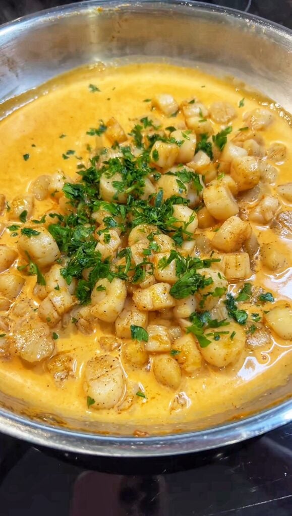 Seared bay scallops in a Cajun cream sauce. The sauce is orangish in color and the dish is garnished with fresh chopped parsley.