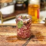 A jar of quick pickled red onions with bay leaves and peppercorns.