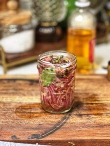 A jar of quick pickled red onions with bay leaves and peppercorns.