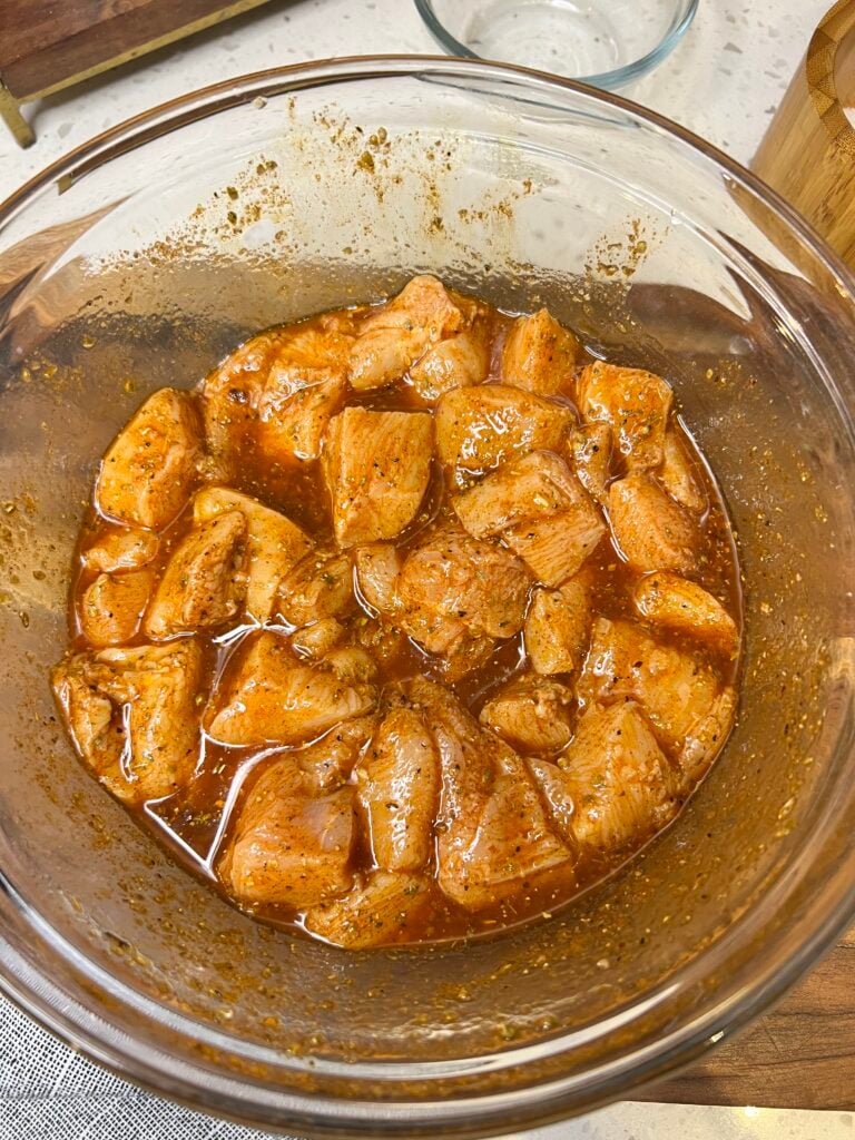 Cubed chicken breasts in a glass bowl with a marinade of olive oil and spices.
