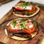 Two pitas filled with homemade doner kebab meat, sliced tomatoes, red onions, tzatziki sauce and fresh parsley.