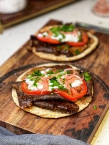 Two pitas filled with homemade doner kebab meat, sliced tomatoes, red onions, tzatziki sauce and fresh parsley.