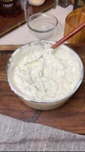 A bowl of creamy homemade tzatziki sauce. The sauce is white with cucumber.