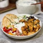 An air fryer Greek chicken bowl with pita, onions, tomatoes, feta cheese, cucumbers, tzatziki sauce and olives.