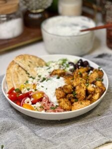 An air fryer Greek chicken bowl with pita, onions, tomatoes, feta cheese, cucumbers, tzatziki sauce and olives.