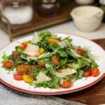 A plate of Pork Milanese with Arugula Salad. Crispy fried pork is topped with an arugula salad with cherry tomatoes and shaved Parmesan cheese.