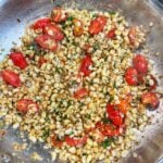 A stainless steel pan of brown butter sweet corn with blistered tomatoes and fresh parsley.