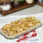 A white platter of lobster roll pasta salad. Pasta shells are mixed with lobster meat and mayo and topped with a crunchy panko topping.