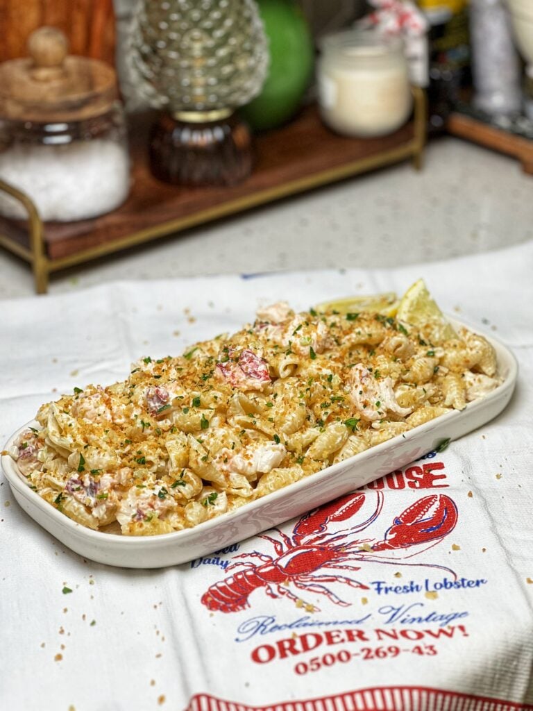 A white platter of lobster roll pasta salad. Pasta shells are mixed with lobster meat and mayo and topped with a crunchy panko topping.