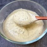 A creamy Parmesan peppercorn salad dressing in a glass bowl. The photo is showing a spoonful of the dressing.