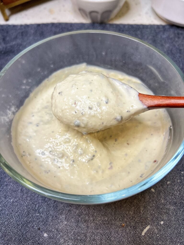 A creamy Parmesan peppercorn salad dressing in a glass bowl. The photo is showing a spoonful of the dressing.