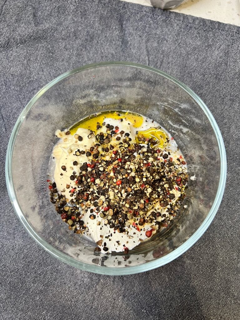 Mayo, sour cream, olive oil, and coarse ground peppercorns in a glass bowl for Parmesan Peppercorn salad dressing.