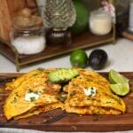 A shrimp fajita quesadilla cut into four wedges and topped with sour cream, cilantro and avocado. Flour tortillas are filled with a cheesy shrimp mixture and toasted until golden brown. Two lime wedges are served on the side.