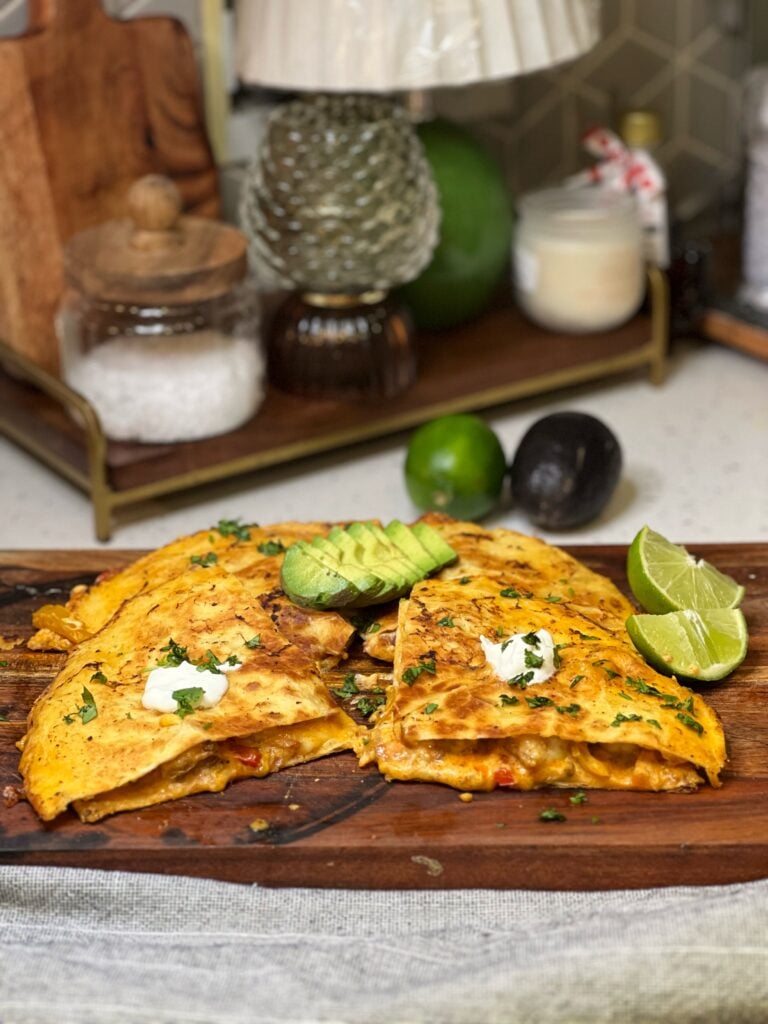 A shrimp fajita quesadilla cut into four wedges and topped with sour cream, cilantro and avocado. Flour tortillas are filled with a cheesy shrimp mixture and toasted until golden brown. Two lime wedges are served on the side.