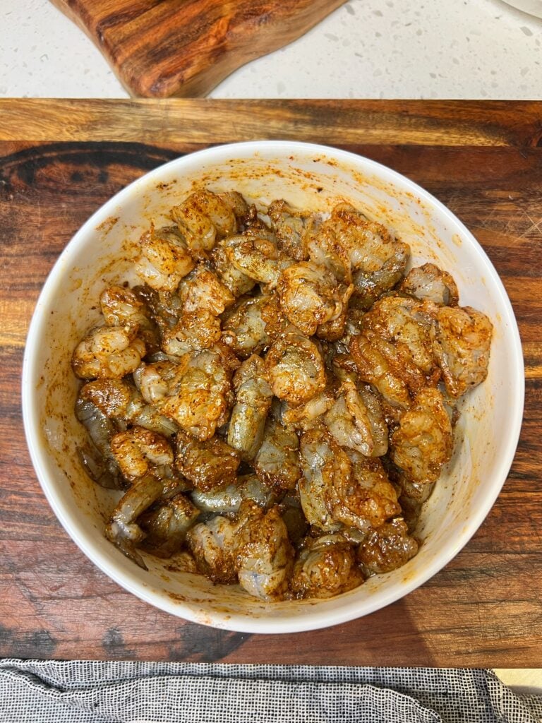 Raw shrimp cut into bite sized pieces coated with olive oil and taco seasoning in a white bowl.